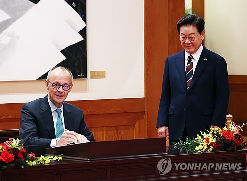 German Chancellor Friedrich Merz (L) writes in a guestbook at Cheong Wa Dae in Seoul on Oct. 29, 2026, as President Lee Jae Myung stands by. (Yonhap)